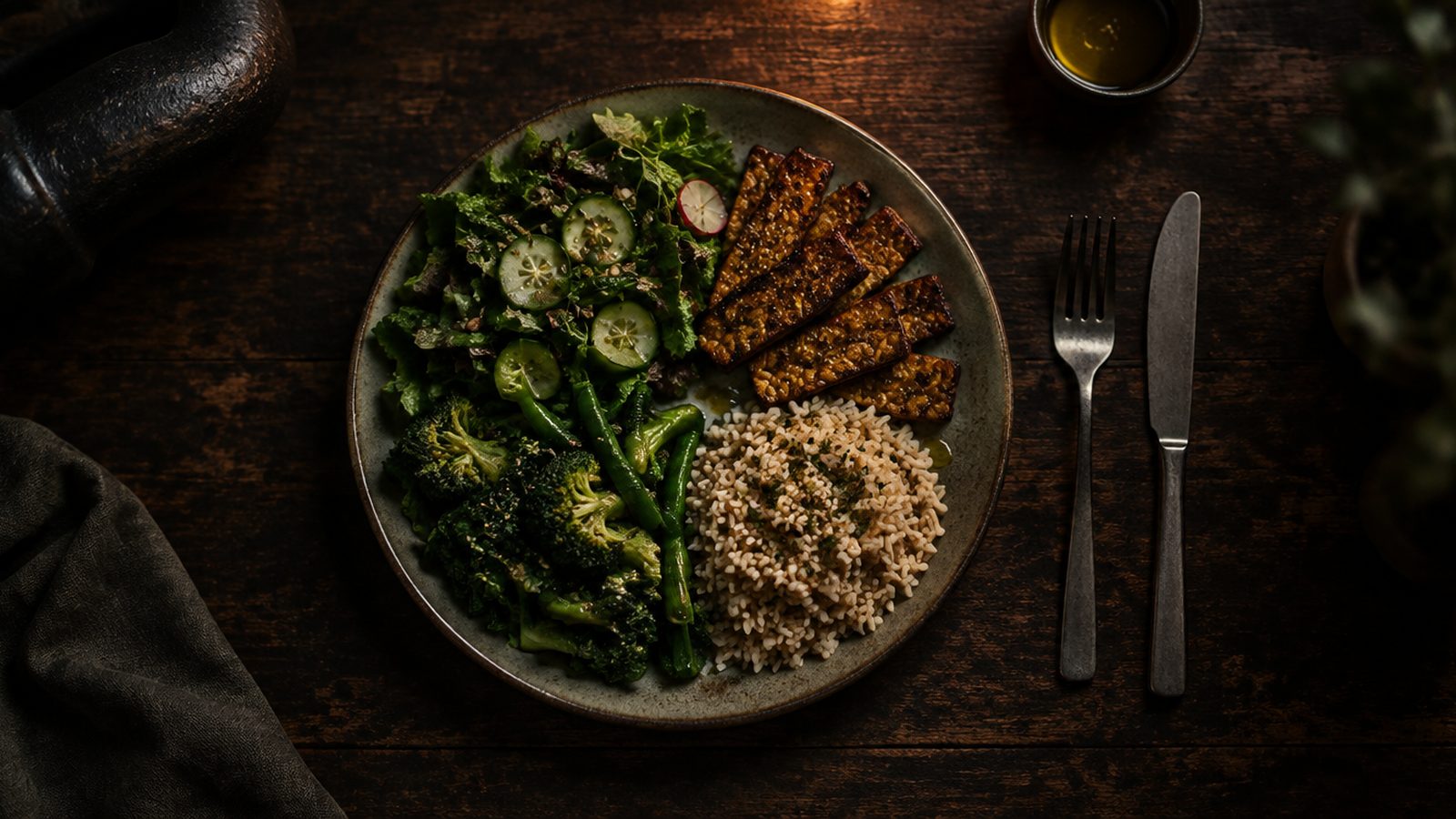 A plate half vegetables with seared tempeh and brown rice on a dark table